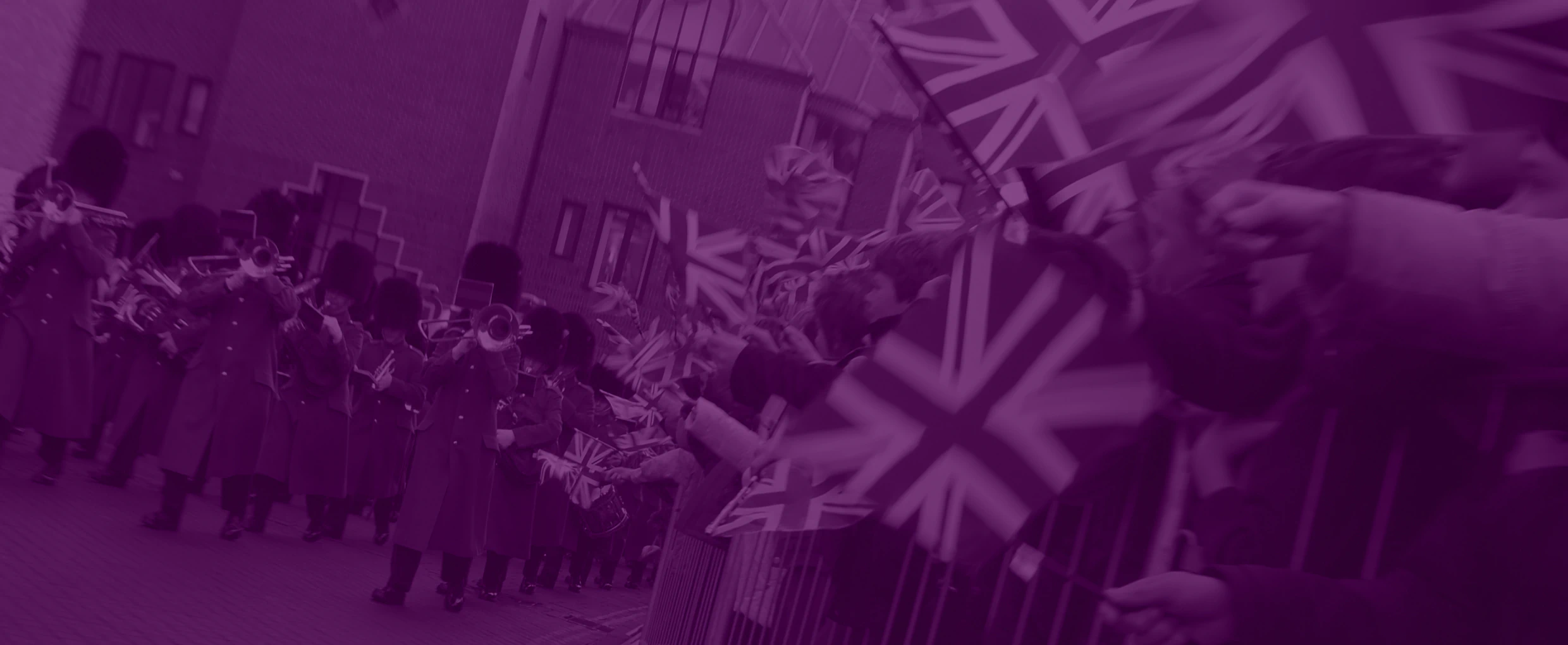 A British armed forces personnel marching band marching past crowds waving Union Jacks.